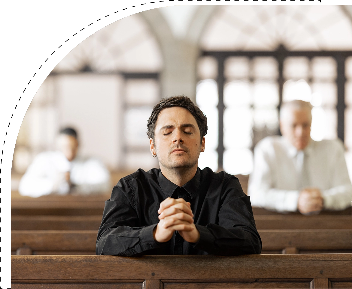 A man sitting in the middle of two pews with his hands folded together.