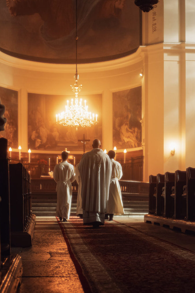 Three men in white robes are standing inside a church.