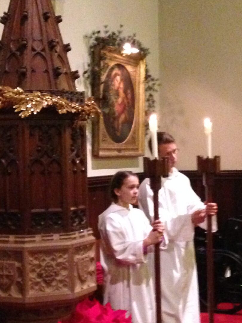 Two people in white robes holding candles and a cross.