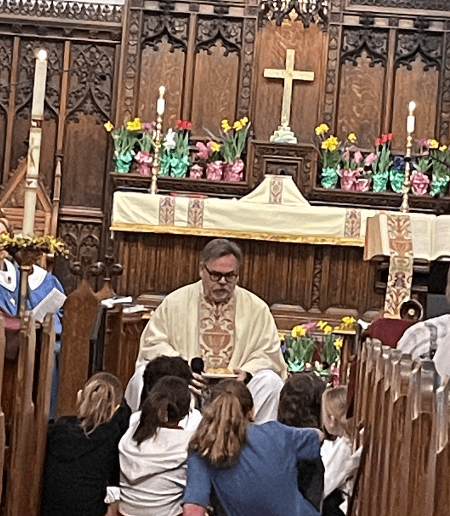 A priest is sitting in front of children.