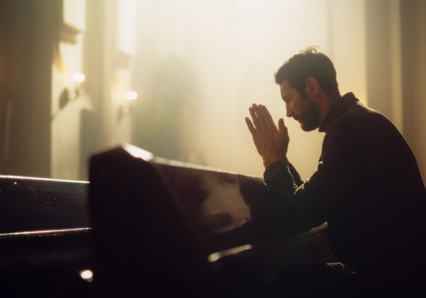 A man sitting in front of a piano with his hands folded together.