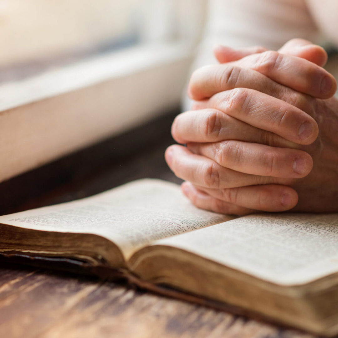 A person with their hands folded over an open book